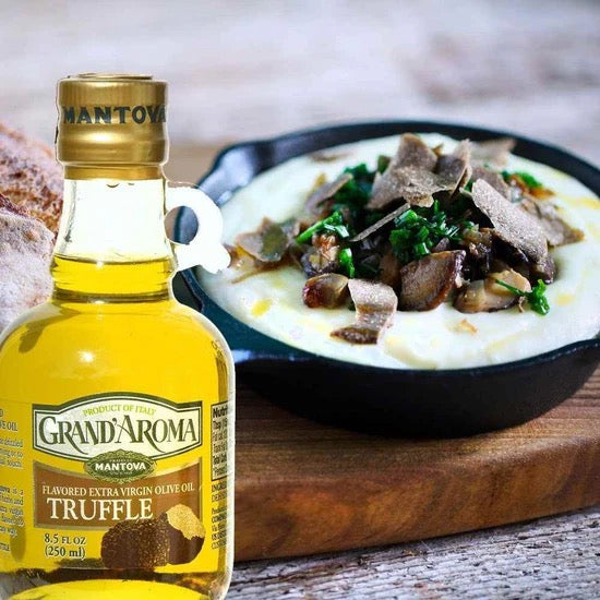 Bottle of Grand'Aroma truffle oil next to a dish with truffled food on a wooden surface.